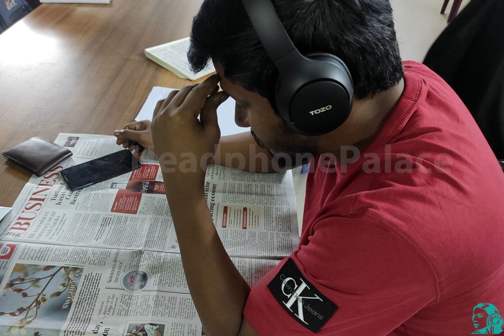 A student reading newspaper in the library and using HT2 Headphone